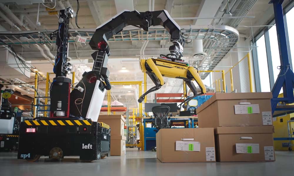 Ein großer Roboter-Greifarm saugt den Hunderoboter Spot von Boston Dynamics an. Der Arm gehört zu Stretch, dem neuen Roboter von Boston Dynamics.