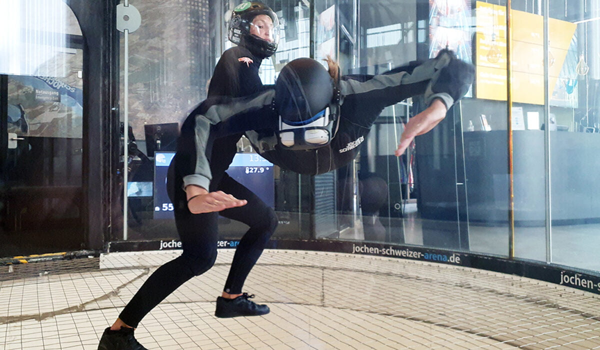 Ein Mann mit VR-Brille schwebt im Windkanal. Eine Frau hält ihn fest.