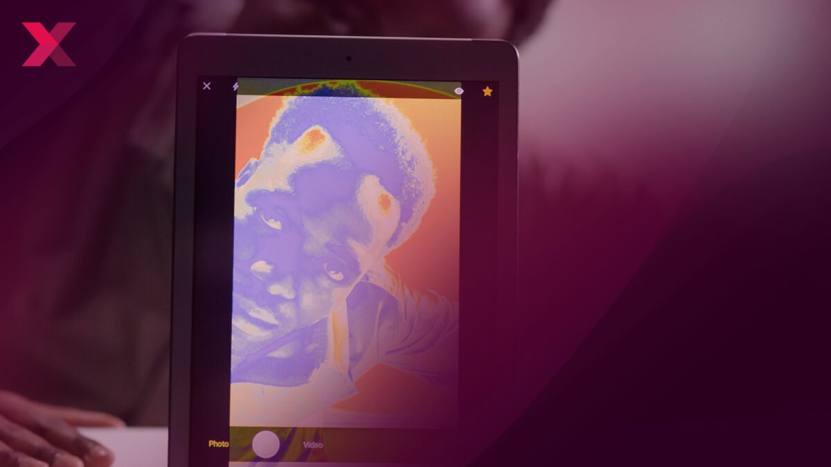 Ein Mann schaut von hinten in eine Smartphone-Kamera, das Smartphone zeigt nach vorne ein farblich verzerrtes Bild seines Gesichts.