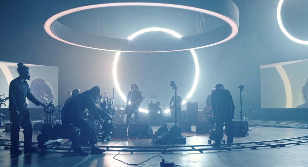 Foo Fighters spielen ein Konzert umgeben von Leuchtringen und einem Kamerateam.