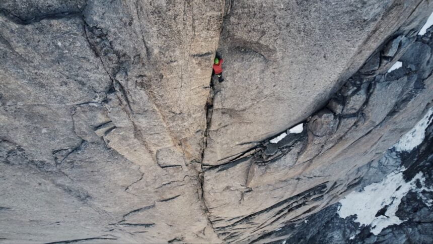 Alex Honnold klettert als winzige rote Figur eine Felsspalte hoch.