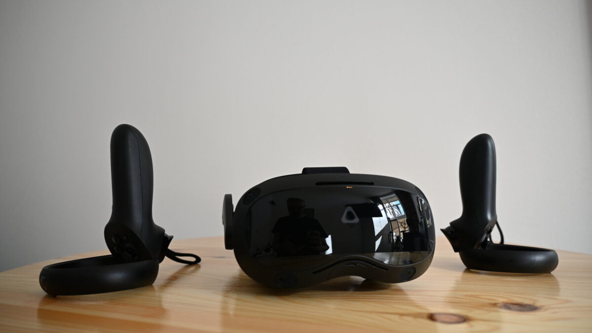 Schwarze VR-Brille Vive Focus 3 von vorn auf Tisch, flankiert von zwei VR-Controllern