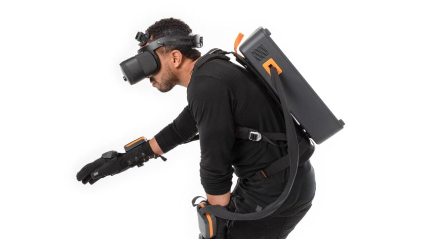 Mann mit Haptx-Handschuhen und -Rucksack greift nach virtuellem Objekt.