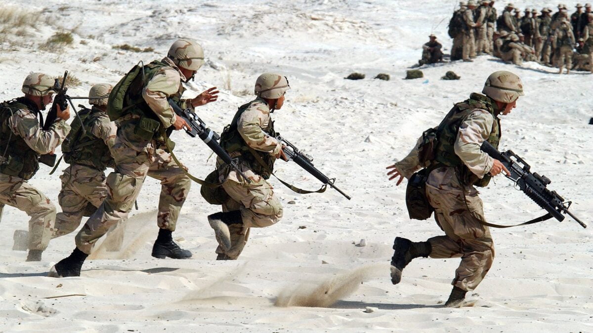Bewaffnete Soldaten rennen in einer Übung über eine Sandlandschaft.