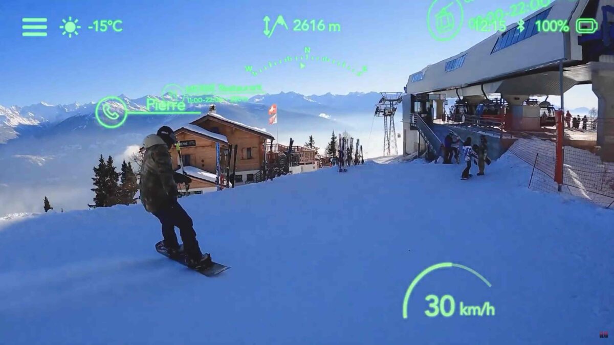 Der Blick durch eine Skibrille mit AR-Display zeigt einen Snowboarder, die Piste und virtuelle Elemente wie eine Geschwindigkeitsanzeige.