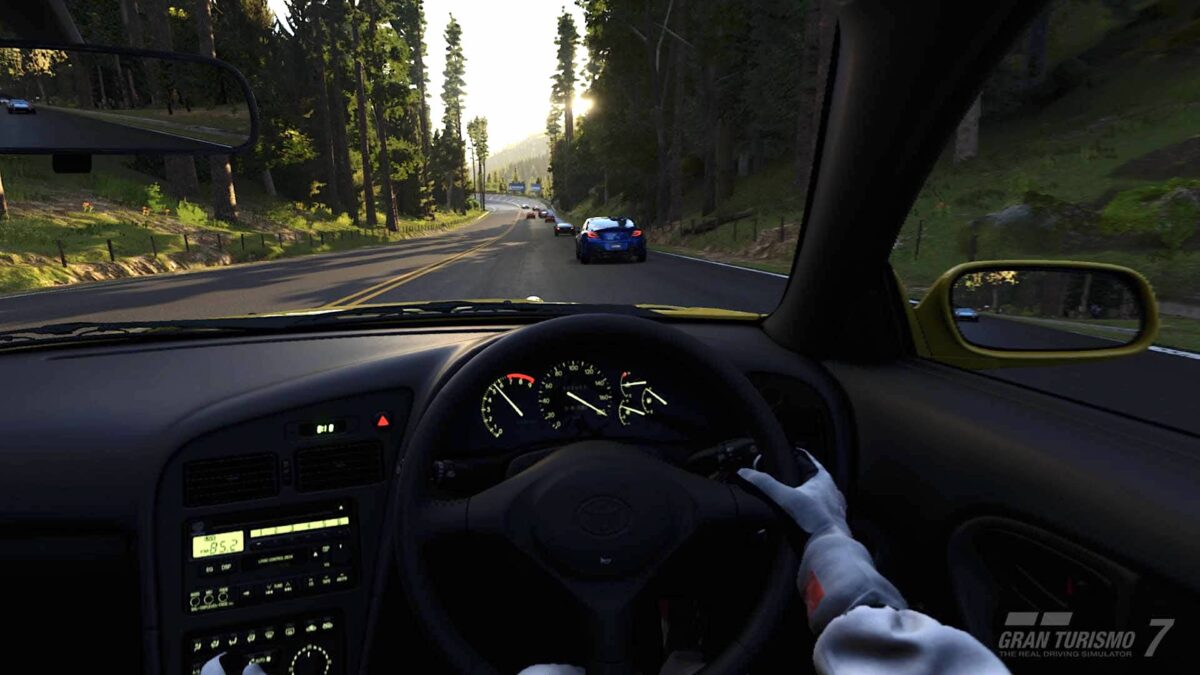 Sicht aus dem Cockpit eines GT7-Rennwagens auf eine zu beiden Seiten von Wald begrenzten Straße.