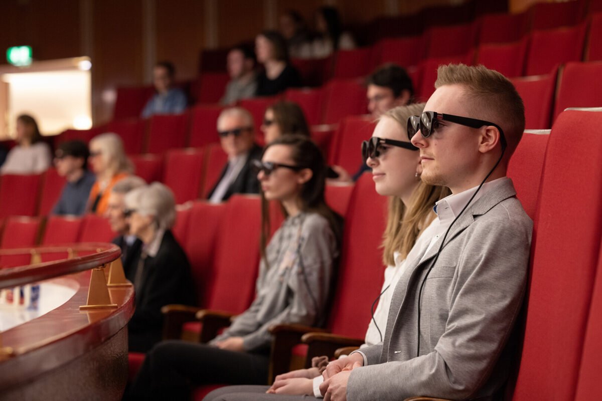 Frauen und Männer mit AR-Brillen sitzen im Zuschauerraum eines Opernsaals.