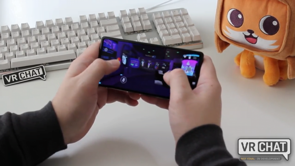 Zwei Hände bedienen auf einem Android-Smartphone VRChat, neben einer Plüschkatze und einer Tastatur.