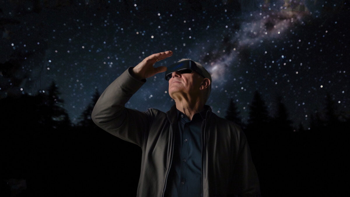 Tim Cook trägt ein XR-Headset, dahinter die Milchstraße und die Sterne.