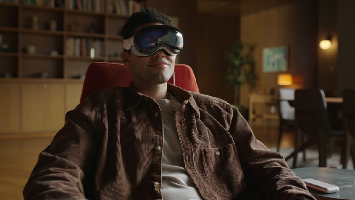 Ein Mann sitzt mit einem Grinsen im Gesicht und der Apple Vision Pro auf dem Kopf auf einem Sessel.