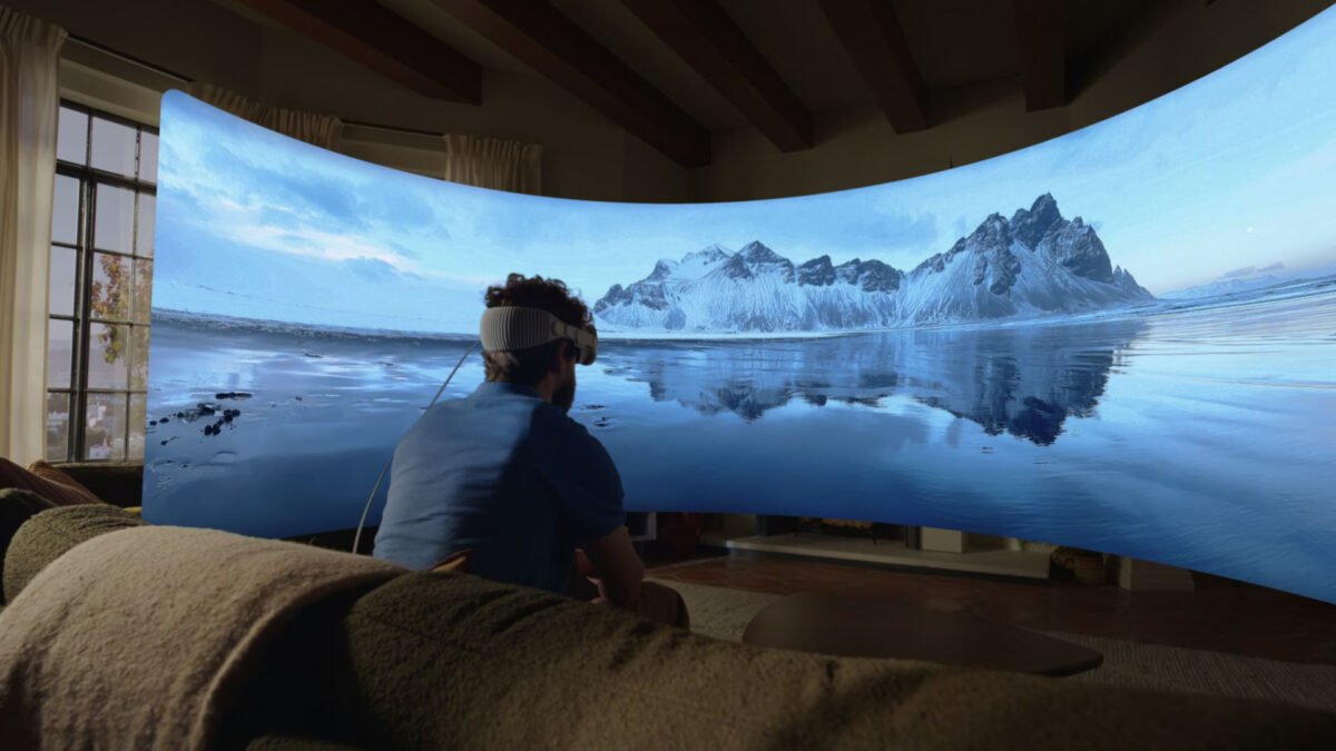 Ein Mann sitzt mit einer Apple Vision Pro auf dem Kopf in seinem Wohnzimmer und blickt auf eine virtuelle Leinwand, die ein Landschaftsbild zeigt.