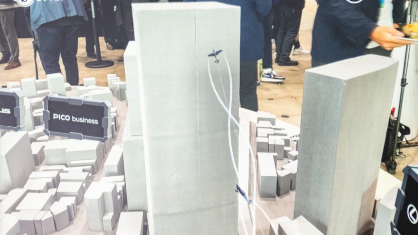 Blick durchs Smartphone auf ein Block-Modell von Shibuya mit AR-Flugzeugen vor einem Wolkenkratzer
