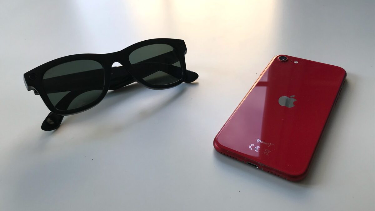Eine Ray-Ban Stories liegt neben einem roten iPhone auf einem Tisch.