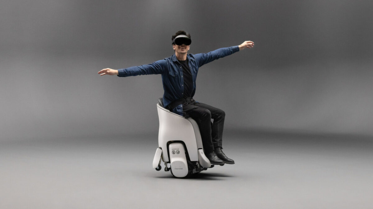Ein Mann sitzt mit ausgestreckten Armen und einer VR-Brille auf einem Fahrroboter von Honda.