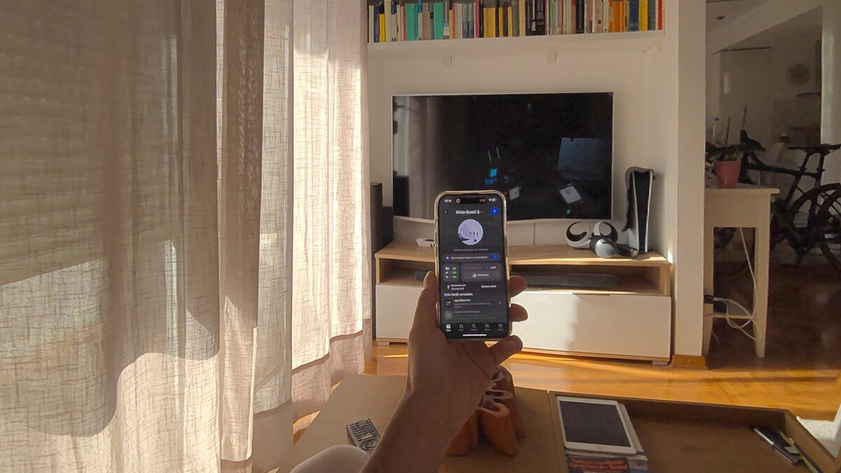 Passthrough-Ansicht eines Wohnzimmer mit Quest Update 64. Der Nutzer hält ein Smartphone vor sich hin.