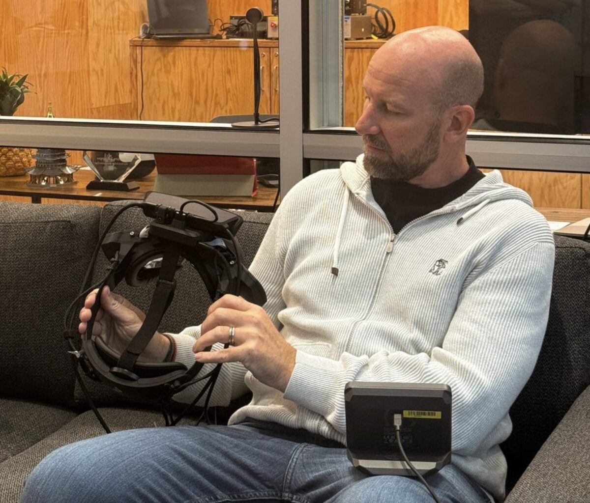 Bosworth sitzt auf einer Couch und sieht sich den Wide-Fov-Prototyp einer VR-Brille an.